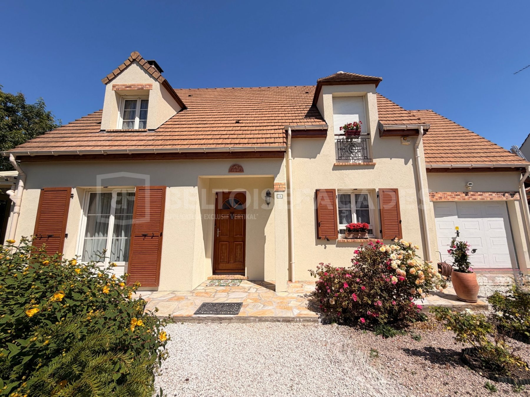 Maison avec façade rénovée par Beltoise Façades, volets marron et jardin fleuri.